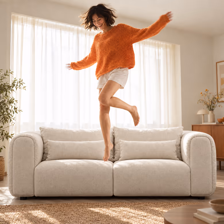A woman in an orange jumper leaping above the cream Luma sofa