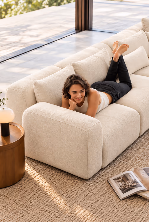Claire lying on a cream Luma sofa by a sunny window