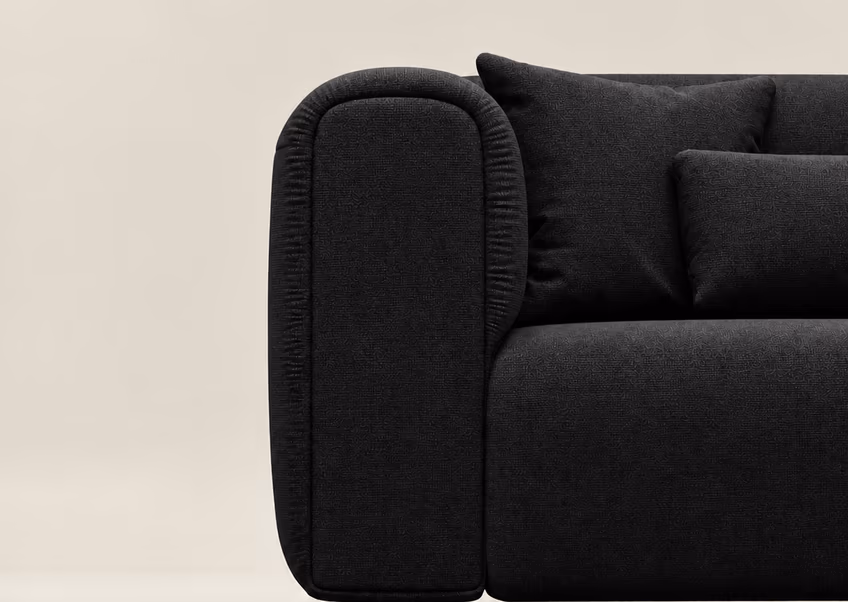 The arm of the charcoal Luma sofa against a pale wall